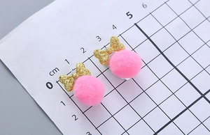 Detailed close-up showing pink pompom earrings with gold glitter bows on a scale ruler