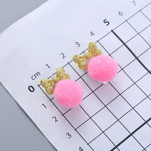Pink pompom earrings with golden glitter bows on a scale measuring grid for children