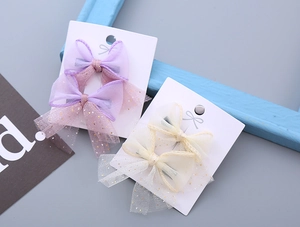Detail view of sweet mesh bow hair clips in lavender and cream with golden sequins