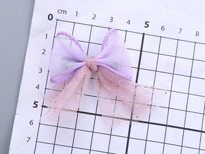 Detail of light purple mesh bow hair clip with gold dots on a cm measuring grid