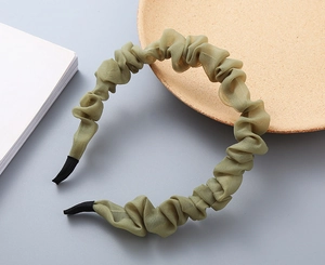 Dettaglio del cerchietto in organza verde oliva plissettato su vassoio in legno