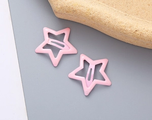 Gros plan de deux barrettes en métal rose en forme d'étoile sur fond gris