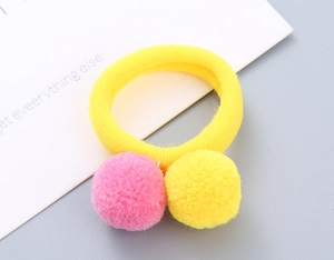 Detailed macro view of yellow elastic hair tie with soft pink and yellow pom-poms for girls