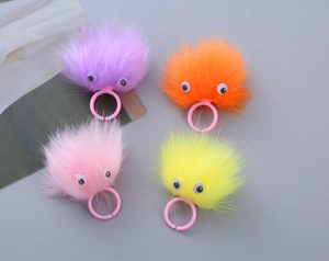 Detail of four colorful plush monster rings with googly eyes and pink plastic bands