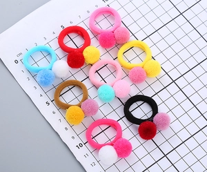 Close-up of eight colorful children's hair ties with soft pom-poms on a measuring scale