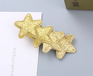 Detail of a gold glitter star hair clip with four sequins stars on a black metal base