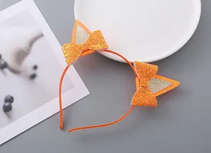 Dettaglio del cerchietto con orecchie di gatto arancione glitterato e fiocco per capelli