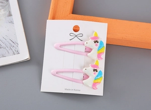 Detalle de pinzas para el pelo de unicornio en resina con purpurina sobre cartón blanco