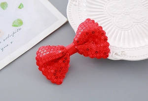 Detail of red sequined bow hair clip with wavy edges and glittery finish on a white plate