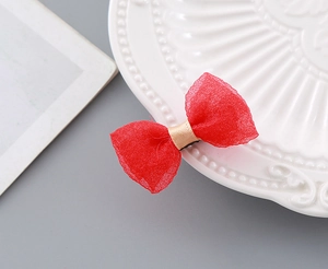 Detailed close-up of a festive red mesh bow hair clip on a vintage white porcelain plate