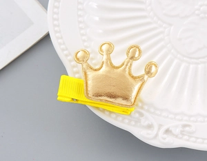 Macro shot of a golden textured crown hair clip with yellow ribbon on a ceramic plate