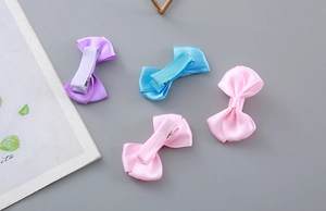 Detailed view of four colorful satin bow hair clips for kids on a minimalist grey background