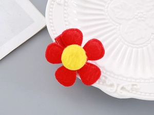 Detailed macro of red plush flower hair clip with yellow pom-pom and duckbill clip