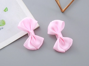 Macro detail showing a pair of glossy pink satin bow hair clips on a minimalist background