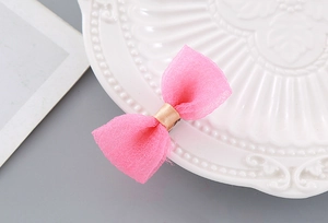 Detail of pink mesh bow hair clip with gold ribbon center on white ceramic plate