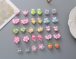 Flat lay of colorful resin clip-on earrings for kids featuring glittery flower and crown shapes
