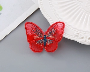 Detail of red butterfly hair clip with embroidery texture and intricate gold thread wing patterns