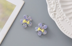 Detail showing two purple resin flower hair clips with glitter and yellow bows