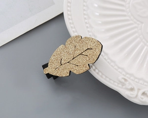 Detailed view of leaf-shaped hair clip with golden glitter finish on a white plate