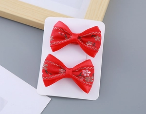 Detail of red silk bow hair clips with cherry blossom embroidery on a display card