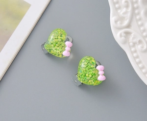 Macro detail of heart-shaped glitter resin ear clips with pink bows for children
