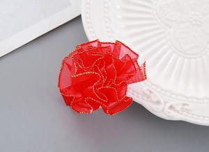 Detail of red floral hair clip with gold-edged organza petals on a white ceramic plate