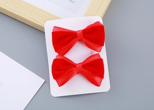 Pair of red plush bow hair clips with rhinestones on a white display card for New Year