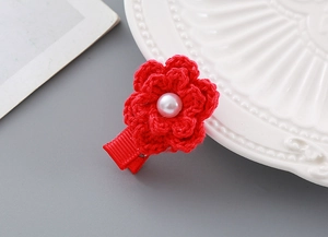Close-up of red crochet flower hair clip with white pearl center and ribbon wrap