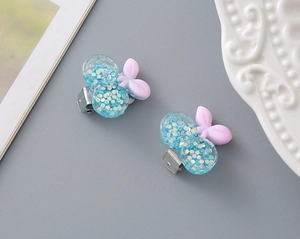 Close-up of glittery blue berry-shaped resin hair clips with purple bows on a ceramic plate