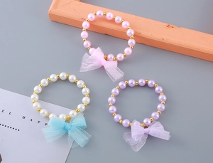 Detail of children pearl bracelets set with mesh bow charms in pink white and purple