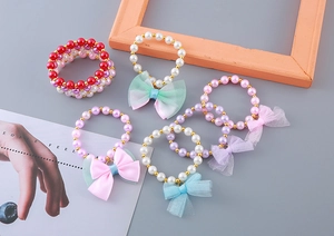 Close-up of girls' pearl bracelets featuring colorful satin bows and gold beads