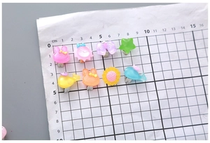 Détail de clips animaux en résine colorée sur papier quadrillé montrant la taille réelle
