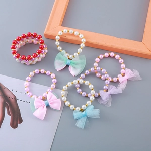 Colorful girl's pearl bracelet set with ribbon bows and golden beads on grey background