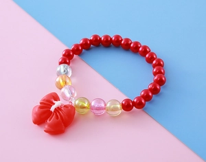 Close-up of children's beaded bracelet featuring red glossy beads and a cute bow pendant