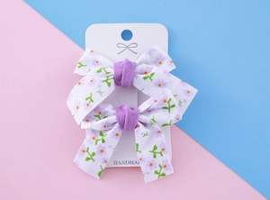 Détail de deux barrettes à fleurs faites à la main avec petits motifs violets et nœuds