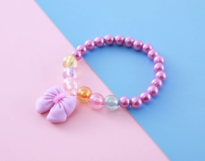 Macro detail of children's bracelet with purple faux pearls and a matte bow charm
