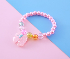 Detail of children's pink faux pearl bracelet with a cute resin bow pendant