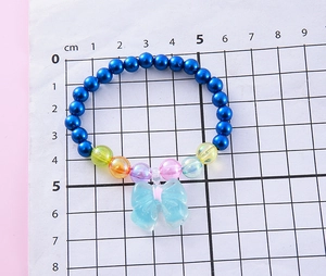 Close-up of blue beaded bracelet for girls with colorful bow resin pendant on grid paper