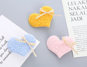 Detail of plush heart-shaped hair clips in yellow, blue, and pink with ribbon bows