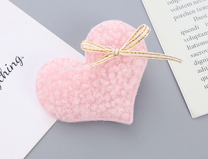 Close-up of pink heart-shaped plush hair clip with lamb wool texture and white bow decoration