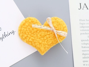 Close-up of heart-shaped yellow teddy velvet hair clip with a gold striped white bow