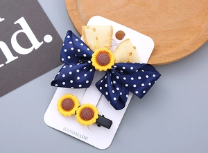Detail view of handmade navy blue polka dot bow hair clip set with sunflower and cherry motifs
