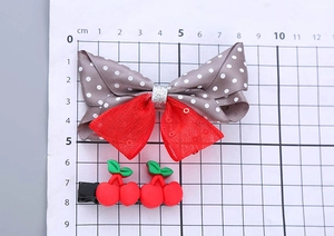 Detail view of polka dot bow and cherry hair clips on a measuring tool showing size