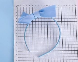 Detailed view of light blue oversized bow headband showing size measurement on scale paper