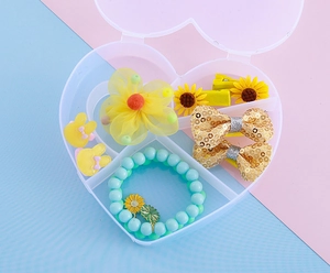 Détail de barrettes fleurs et bracelet de perles dans une boîte de rangement en cœur