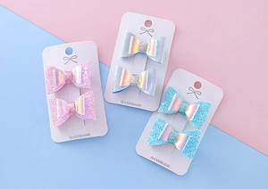 Détail macro de trois paires de barrettes à nœuds pailletées sur cartes blanches