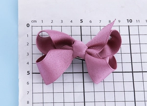 Detail view of a 8.5cm dusky pink ribbed bow hair clip on a measurement grid paper
