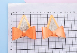 Détail de pinces à cheveux oreilles de chat pailletées orange avec nœuds sur règle