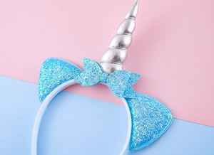 Détail des oreilles de licorne pailletées bleues et corne argentée sur un serre-tête de fête