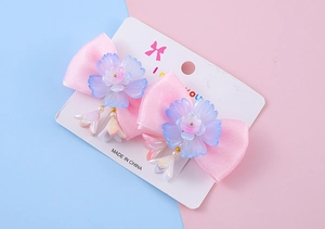 Détail de pinces à cheveux roses avec fleurs en résine violette et pompons dégradés